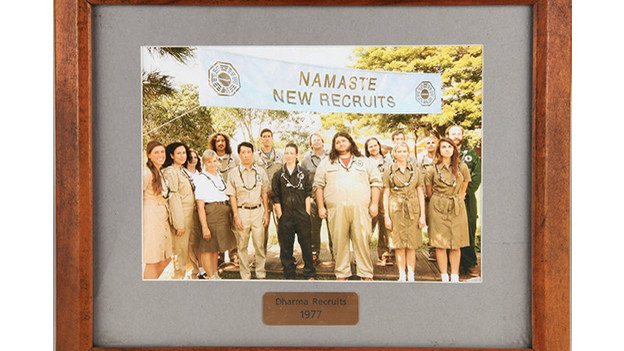 Framed group photo of the 1977 DHARMA recruitsThe photograph shows the 16 new DHARMA recruits from 1977, featuring prominently Jack, Kate and Hurley, who somehow landed on the Island in that year while on board the Ajira Airways Flight 316 to Guam, with Frank Lapidus as the pilot, in the episode, "Namaste."Related content:EPISODE RECAP - "Namaste"PHOTOS - "Namaste"EPISODE RECAP - "Follow the Leader"