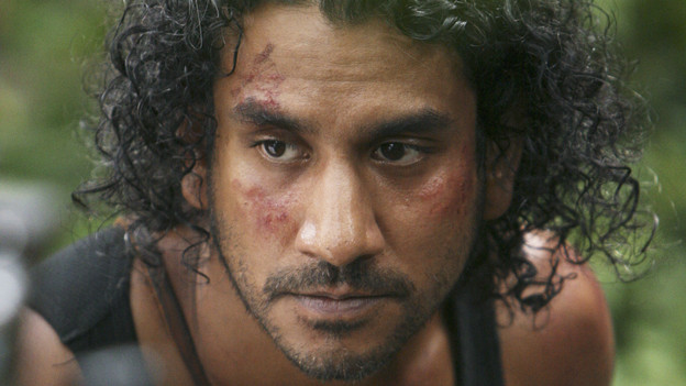 Close-up of Sayid on the island with blood and bruises on his face, wearing a black tank top.
