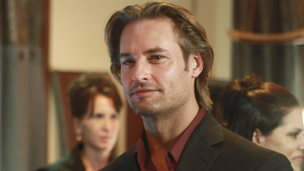 LOST Screencap. Close-up shot of Sawyer in a restaurant wearing a deep red, collared shirt and black suit jacket. Two women appear in the background.